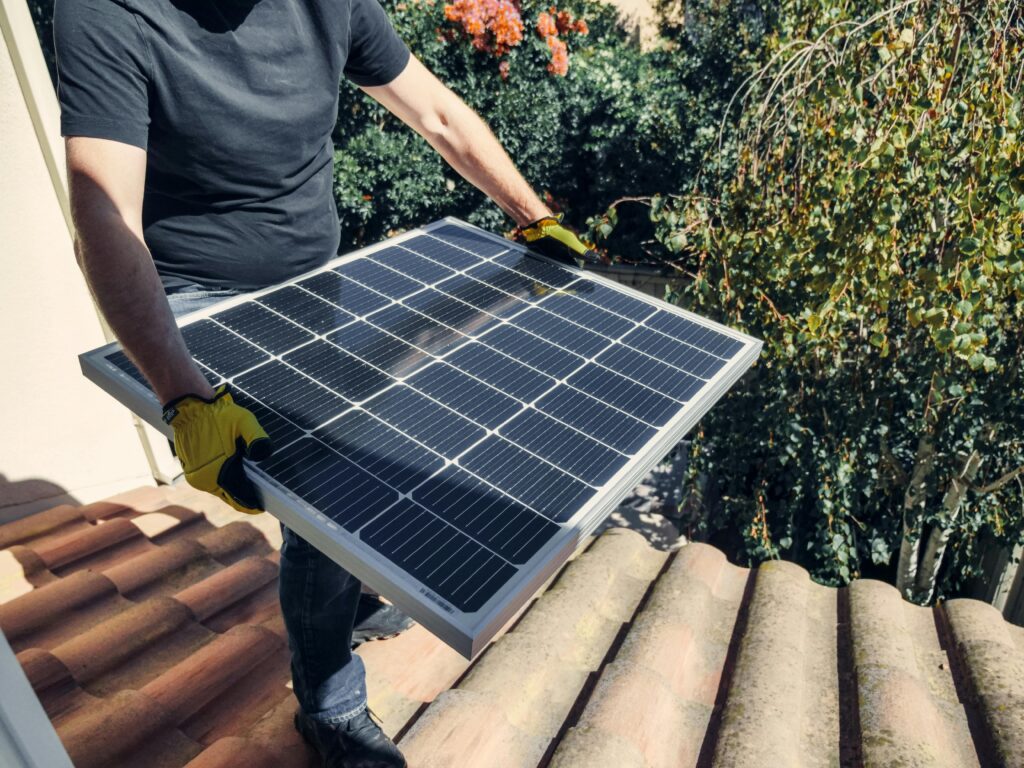 A worker installs a solar panel on a rooftop amidst lush greenery.